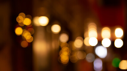 Abstract evening night shimmering bokeh background effect outside near cafe restaurant. Defocused urban city life blur golden light bulbs wreath garlands. Christmas New Year party holiday concept

