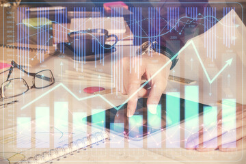 Double exposure of man's hands holding and using a digital device and forex graph drawing. Financial market concept.