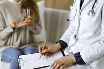 Unknown woman-doctor and patient discussing current health examination while sitting indoors. Stay...