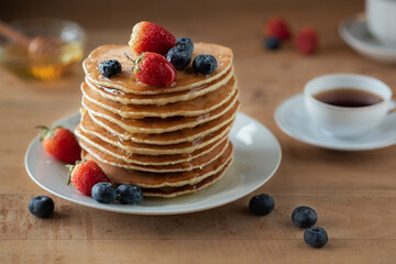 A stack of pancakes on a white plate with strawberries and blueberries on a wooden table