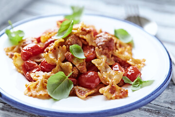 Farfalle pasta with chicken breast, cherry tomatoes and fresh basil. Bright wooden background. Close up.