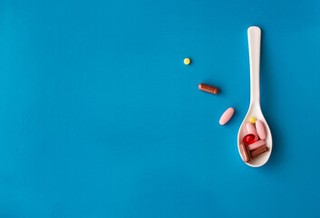 Different colors medical pills on the white spoon without  form  on blue background with copy space. 