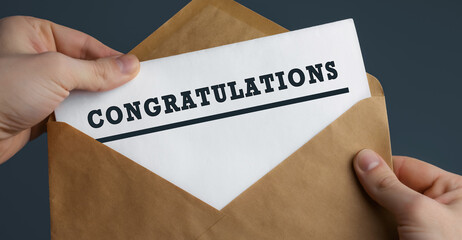 Male hands holding craft envelope with word CONGRATULATIONS on blue background