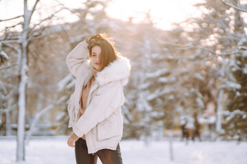 Young beautiful woman  posing in a snowy park. Cold weather. Winter fashion, holidays, rest, travel concept.