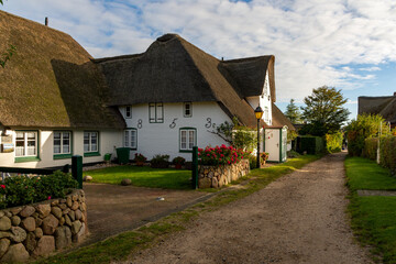 Fototapeta na wymiar Amrum, Germany - October 17, 2020: Small path with thatched houses at a sunny autumn day