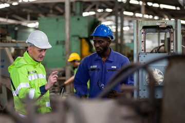 Two engineering male factory workers working and discussing in the industrial factory while wearing safety uniform and hard hat