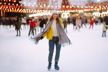 Happy woman ice skating on the ice arena in the city square on Festive Christmas fair. Cold...