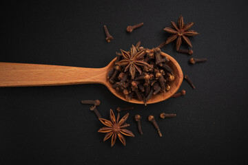 Cloves and anise stars on wooden spoon on dark background.