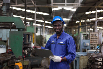 Black male factory mechanic. Happy African American male engineer working or using computer laptop for checking machinery in industry factory and wearing safety uniform and helmet