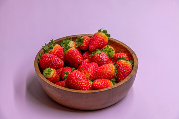 Fresh red strawberries in wooden bowl side view. Strawberry fruits on purple background. Organic food theme.