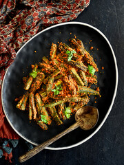 Bhindi Masala or Fried Okra. Indian masala curry on a black background with a wooden spoon.