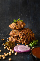 Vegan burger patties with mashed beans, of varying sizes on a dark background with onions, soy beans and tomato sauce. Meatless, restaurant, home chef, cooking concept.