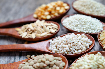 Dry organic pearl barley seeds in wooden spoon with blur other cereal and grain seeds consisted of lentils, rice, sesame,  and quinoa, on grunge background, for healthy food ingredient concept