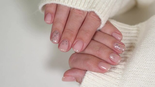 Closeup view 4k video of two manicured female hands isolated on white background. Fingernails painted in pink pastel color and shiny silver glitter.
