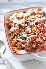 Pasta gratin. Baked fusilli pasta with cherry tomatoes, olives and mozzarella cheese. Bright wooden background. Close up. 