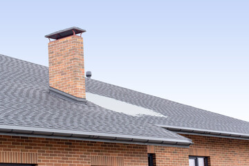 Part of wall made of the brown brick, fragment of roof of modern private dwelling house against of sky