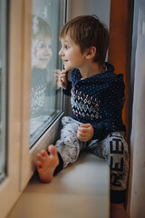 cute little caucasian boy with funny face expression staying home and sitting on window sill looking outside. Image with selective focus