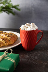 hot chocolate with marshmallow, Green gift box with tag, Christmas tree and croissants on the plate. black background