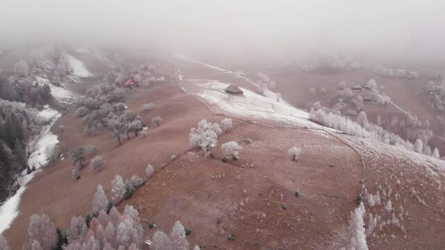 Aerial view of wintertime scene in the Transylvanian village, Pestera, with white frost, fresh snow, blizzard, and fog, at the foot of the Carpathian Mountains