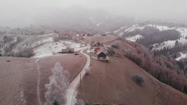 Aerial view of wintertime scene in the Transylvanian village, Pestera, with white frost, fresh snow, blizzard, and fog, at the foot of the Carpathian Mountains