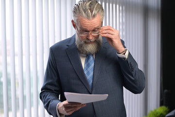The mature gray-haired company executive examines the reports and shakes his head in accusation....