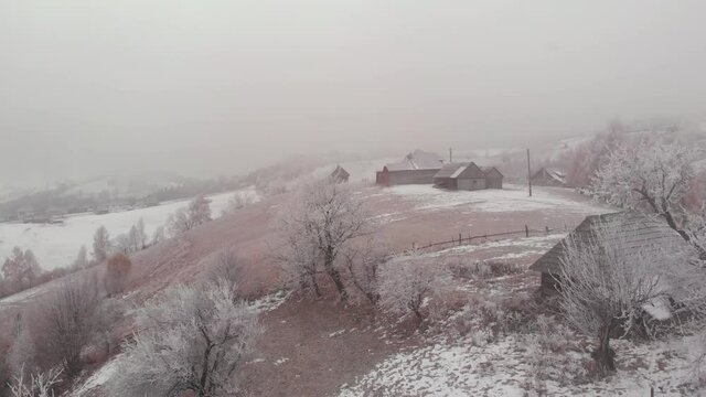 Aerial view of wintertime scene in the Transylvanian village, Pestera, with white frost, fresh snow, blizzard, and fog, at the foot of the Carpathian Mountains