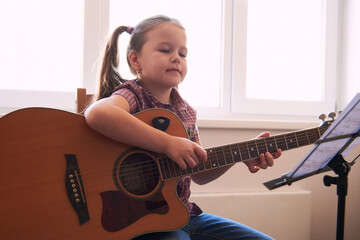 a little girl learns to play the guitar from notes. Music school for children.Musical notation.