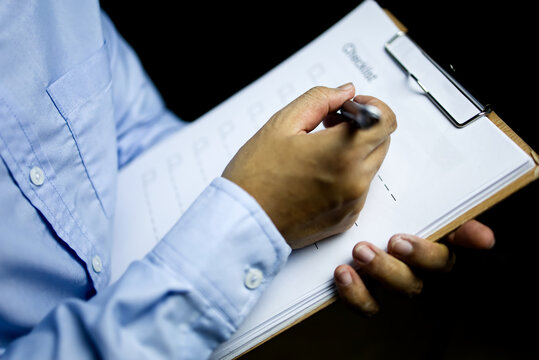 Businessman Holding A Clipboard And Writing The Check List After Product Recieved On The Black Background.