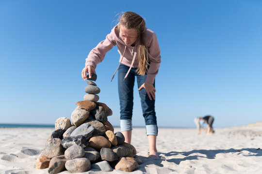ein junges M&auml;dchen baut am Ostseestrand eine Steinpyramiede im Sand bei Sonnenlicht