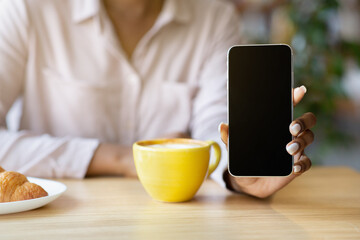 Cropped view of young black woman showing cellphone with blank screen at cafe, space for website design