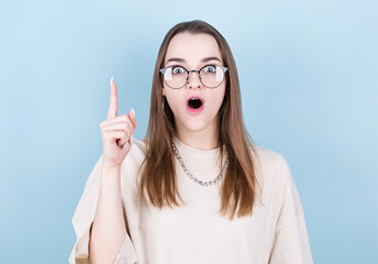 Close-up portrait of charming young woman in eyeglasses pointing with finger, looking at camera, isolated on blue background