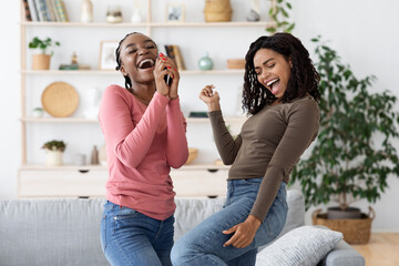 Carefree african american girlfriends singing and dancing at home