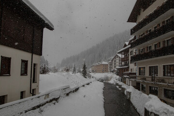 Small river Torrente Frigidolfo in the village of Santa Caterina in heavy snowfall. Visible hotels and houses with some snow flakes falling down.