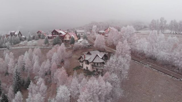 Aerial view of wintertime scene in the Transylvanian village, Pestera, with white frost, fresh snow, blizzard, and fog, at the foot of the Carpathian Mountains