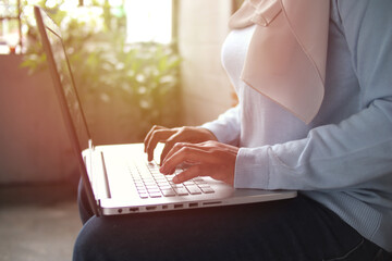 Naklejka premium Asian muslim woman wearing hijab smiling while typing on her laptop, work from home concept