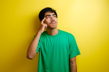 Asian young man in green t-shirt looked happy thinking and looking up, having good idea