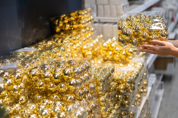 Woman holding packaging of golden balls of decorations on christmas tree in store