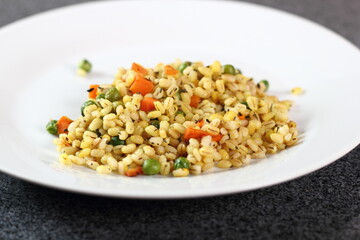 Cooked pearl barley with carrot and green peas on plate