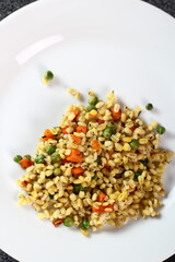 Cooked pearl barley with carrot and green peas on plate
