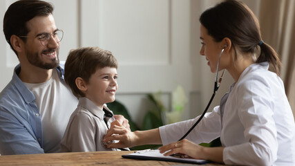 Female pediatrician listen to small boy patient heart chest with stethoscope at consultation with dad. Woman doctor do regular checkup examine little child at clinic with father. Healthcare concept.