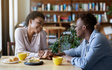 Romantic black couple having breakfast together at cafe, holding hands and looking at each other, panorama