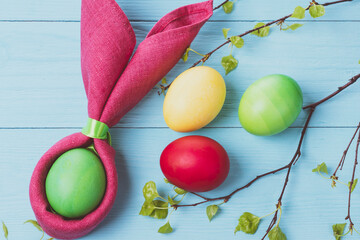 Easter eggs and the shape of rabbit ears and tree branches with green leaves, on a blue wooden background, selective focus, tinted image
