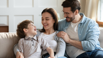 Overjoyed young Caucasian parents have fun relaxing in living room with small preschooler son. Happy family with little boy child laugh enjoy weekend at home, rest on couch together. Bonding concept.