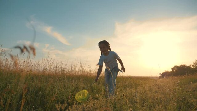 A happy, carefree child runs through a green field, enjoys nature, fresh air. Happy family. The girl is holding a net for catching insects.