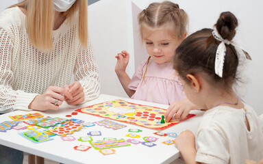 Fototapeta premium A kindergarten teacher plays a board game with two little girls. Mom plays with little daughters