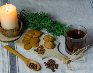 A Christmas table setting with candle, juniper branch, cup of coffee, a coffee grinder, walnuts and cookies
