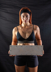 sports girl in mud holds a blank sign in the studio on a black background