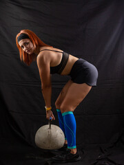Beautiful redhead girl lifts a huge kettlebell in the studio on a black background