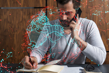 Handsome businessman in casual wears, speaking phone, taking notes at office try to solve global international issue. Double exposure. The concept of international business. Planet hologram.
