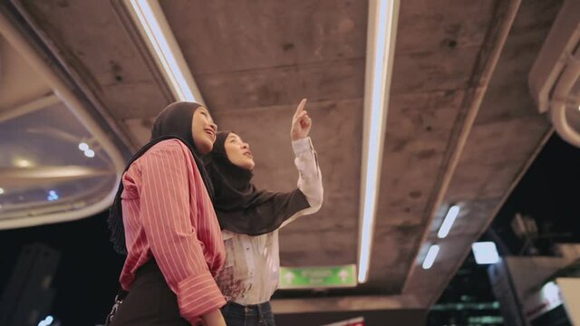 Orbiting shot of Two young female islam friends standing in front of shopping mall, women pointing at map sign, holiday travel vacation, lost tourist community mall people walking by on background